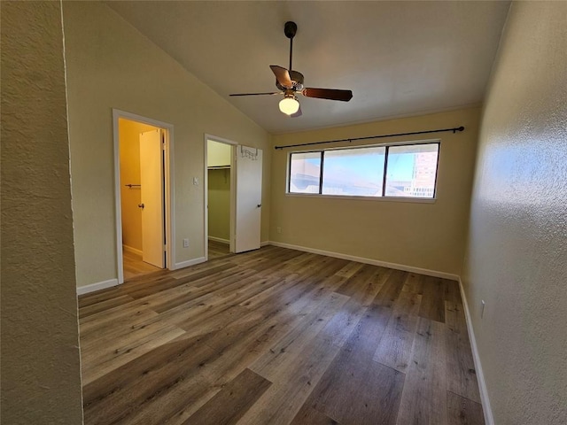 unfurnished bedroom with lofted ceiling, ceiling fan, baseboards, hardwood / wood-style floors, and a walk in closet