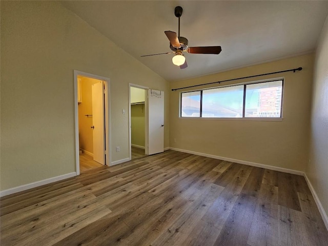 unfurnished bedroom featuring a spacious closet, a ceiling fan, vaulted ceiling, wood finished floors, and baseboards