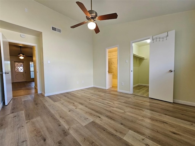 unfurnished bedroom featuring lofted ceiling, a spacious closet, wood finished floors, and visible vents