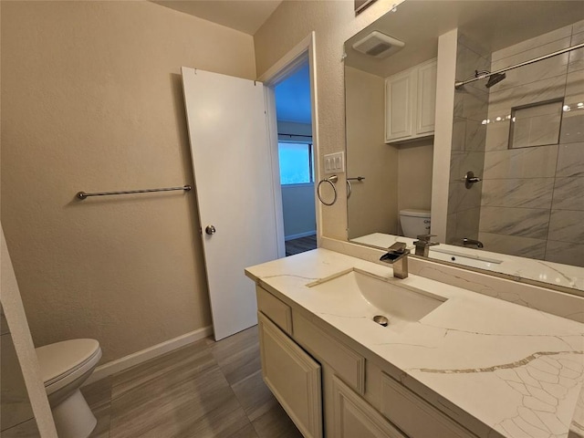 bathroom featuring tiled shower, vanity, toilet, and baseboards