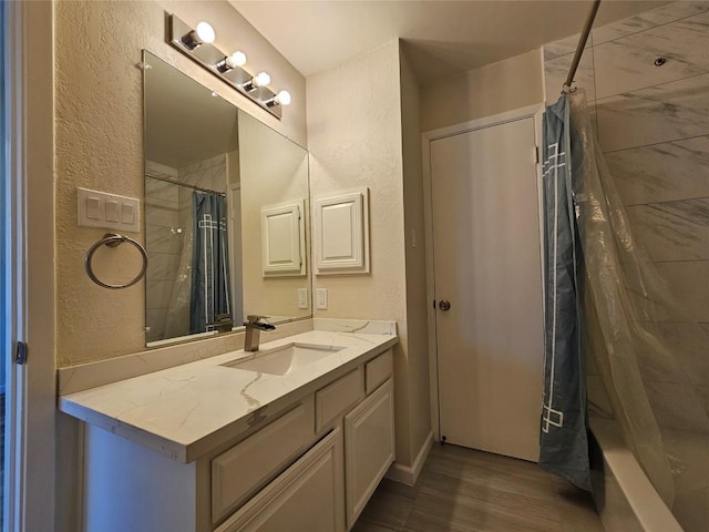 full bath with a textured wall, vanity, a shower with shower curtain, and wood finished floors