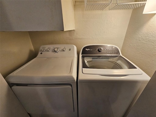 clothes washing area with a textured wall, separate washer and dryer, and laundry area