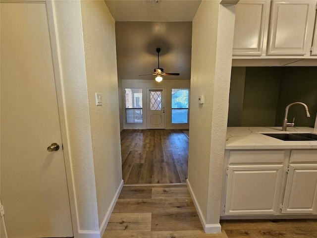 hall with light wood-style floors, baseboards, a sink, and a textured wall