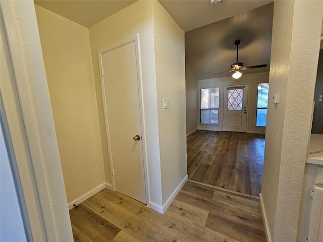 foyer with ceiling fan, a textured wall, baseboards, and wood finished floors