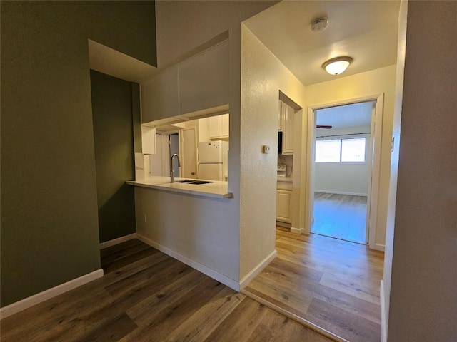 hallway featuring wood finished floors, a sink, and baseboards