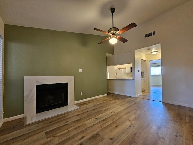 unfurnished living room with visible vents, a premium fireplace, ceiling fan, light wood-type flooring, and baseboards