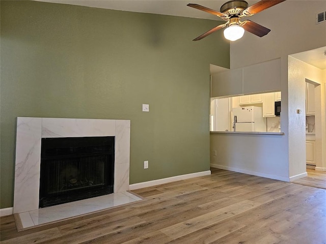 unfurnished living room featuring light wood-style flooring, a fireplace, visible vents, a ceiling fan, and baseboards