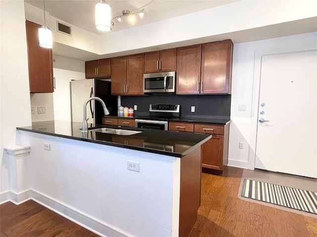 kitchen with dark wood-style floors, stainless steel appliances, visible vents, a sink, and a peninsula