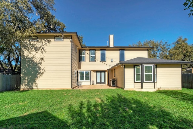 back of property featuring french doors, a fenced backyard, a yard, and a chimney