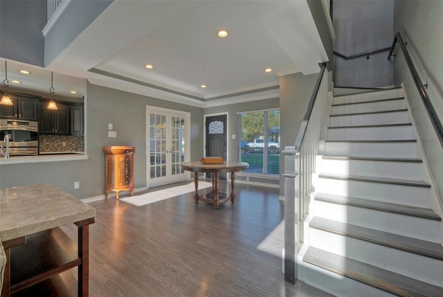 interior space with baseboards, a raised ceiling, wood finished floors, crown molding, and french doors