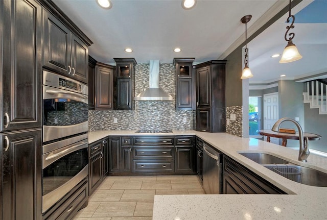 kitchen featuring decorative backsplash, hanging light fixtures, stainless steel appliances, wall chimney range hood, and a sink