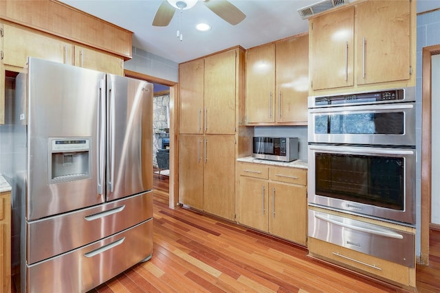 kitchen with a warming drawer, light countertops, appliances with stainless steel finishes, and light wood finished floors