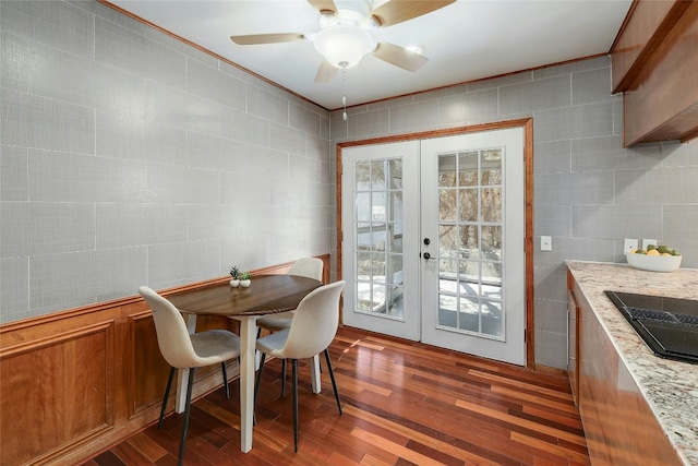 dining room featuring dark wood-style floors, a ceiling fan, tile walls, and french doors