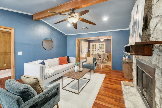 living room featuring vaulted ceiling with beams, visible vents, a fireplace with flush hearth, ornamental molding, and wood finished floors