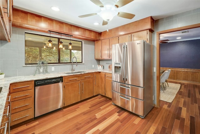 kitchen with appliances with stainless steel finishes, a wainscoted wall, a sink, and light wood finished floors