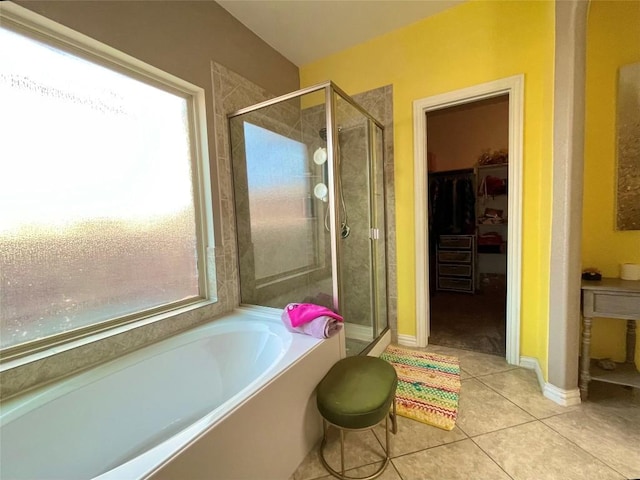 full bathroom featuring tile patterned flooring, a walk in closet, baseboards, a stall shower, and a garden tub