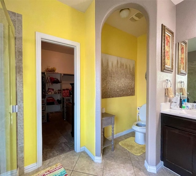 full bathroom featuring tile patterned flooring, vanity, a walk in closet, toilet, and baseboards