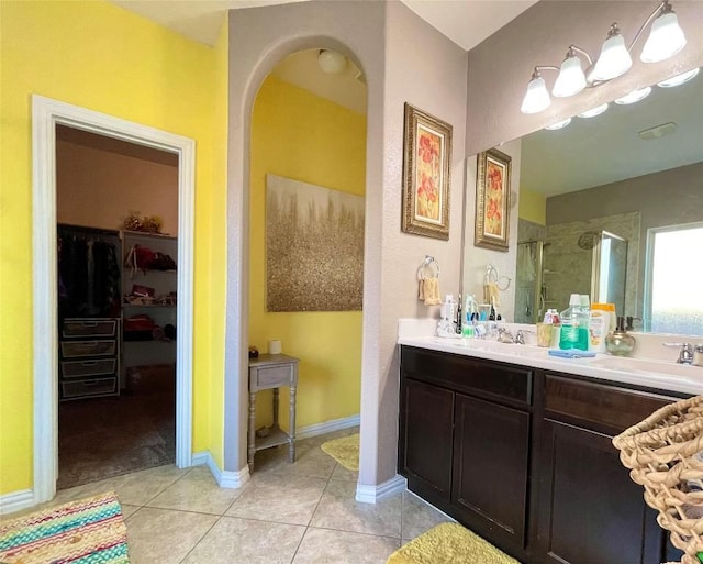 full bath featuring baseboards, tile patterned flooring, a walk in closet, vanity, and a shower stall