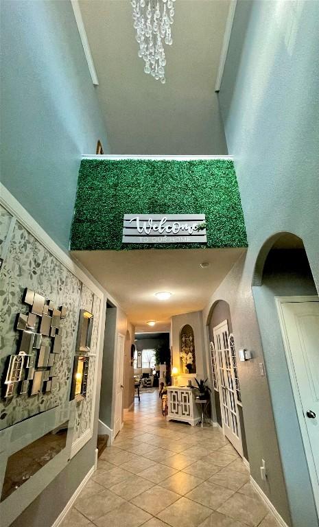 corridor with arched walkways, a towering ceiling, baseboards, and tile patterned flooring