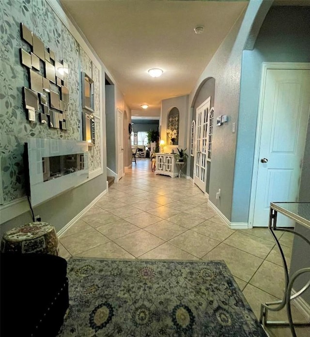 hall with arched walkways, baseboards, and tile patterned floors