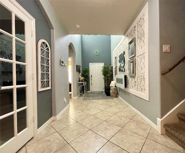 corridor with tile patterned floors, arched walkways, baseboards, and stairs