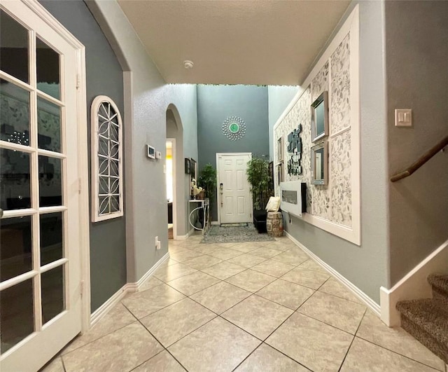 hallway featuring light tile patterned flooring, arched walkways, baseboards, and stairs