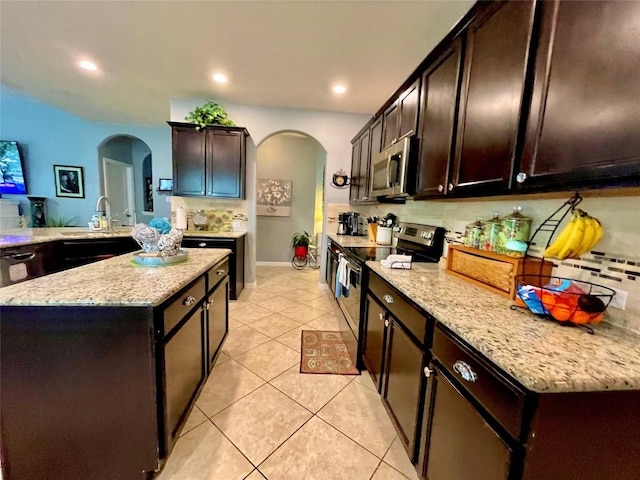 kitchen featuring arched walkways, light tile patterned floors, tasteful backsplash, stainless steel microwave, and range with electric cooktop