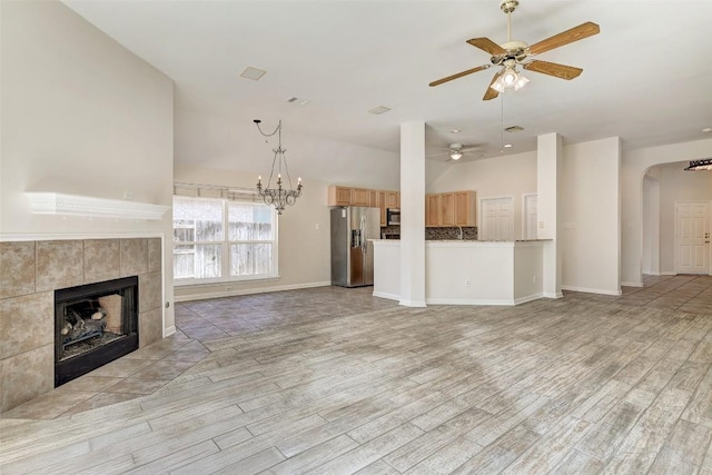 unfurnished living room with arched walkways, light wood-style floors, a tile fireplace, baseboards, and ceiling fan with notable chandelier