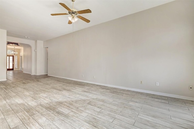 unfurnished room with light wood-type flooring, ceiling fan, arched walkways, and baseboards