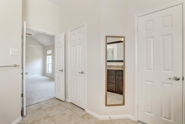 hall with lofted ceiling, baseboards, and light tile patterned floors