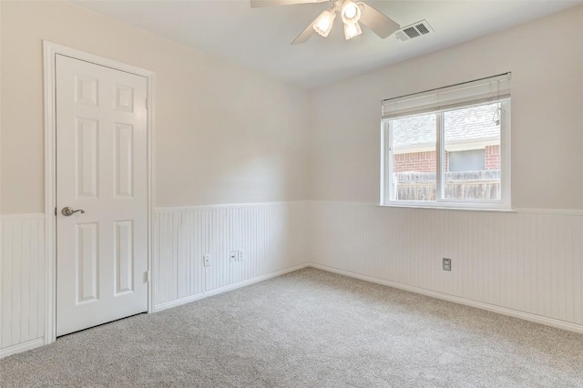 spare room with ceiling fan, visible vents, carpet flooring, and wainscoting