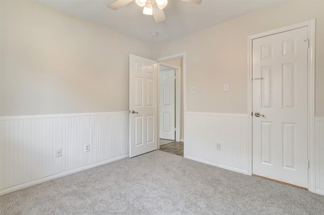 carpeted spare room with a wainscoted wall and ceiling fan