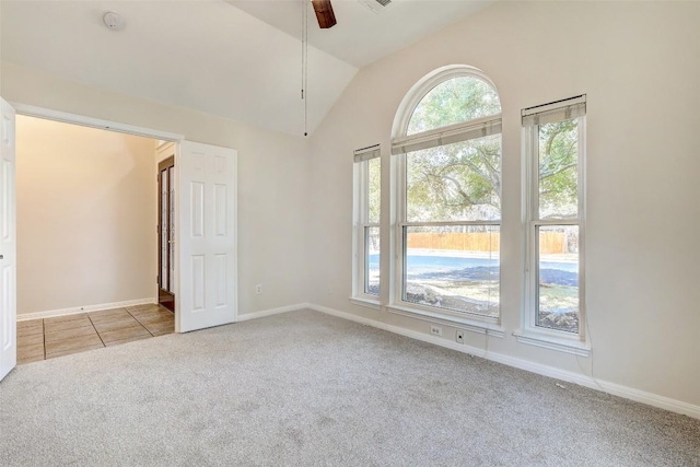 carpeted spare room featuring ceiling fan, vaulted ceiling, baseboards, and tile patterned floors