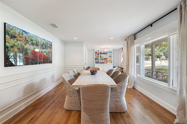 dining room featuring recessed lighting, a decorative wall, wood finished floors, visible vents, and baseboards