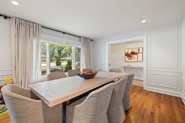 dining room featuring light wood-style flooring, a decorative wall, and recessed lighting