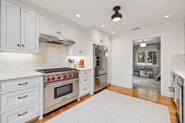 kitchen with under cabinet range hood, light countertops, light wood-type flooring, tasteful backsplash, and high end appliances