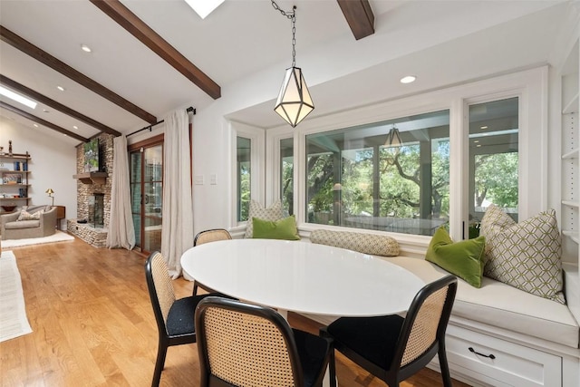 dining space with lofted ceiling with beams, light wood-style floors, recessed lighting, and a stone fireplace