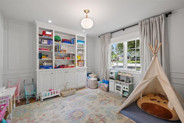 recreation room featuring recessed lighting, a decorative wall, and wood finished floors