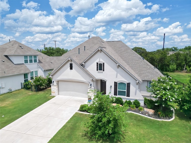 french country home with a front yard, a shingled roof, a garage, stucco siding, and driveway