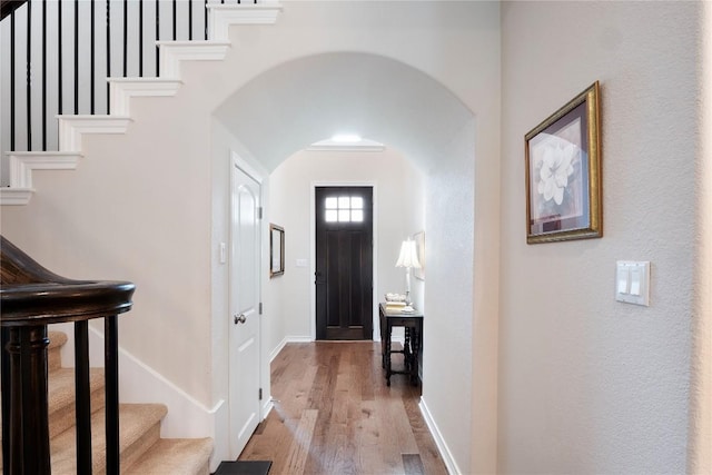 entryway with stairway, baseboards, arched walkways, and wood finished floors