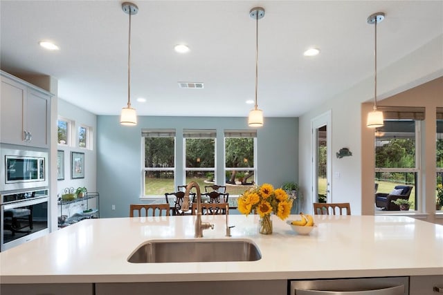 kitchen featuring light countertops, hanging light fixtures, appliances with stainless steel finishes, a sink, and an island with sink