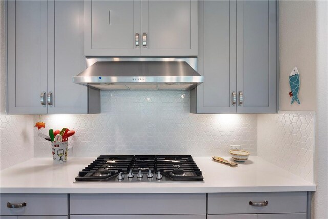 kitchen featuring wall chimney exhaust hood, gray cabinets, light countertops, and stainless steel gas stovetop