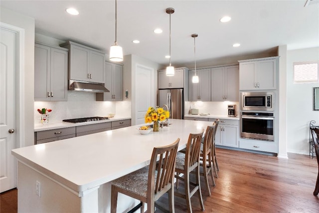 kitchen featuring decorative backsplash, a kitchen island, appliances with stainless steel finishes, gray cabinetry, and under cabinet range hood