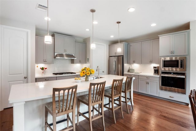 kitchen featuring under cabinet range hood, dark wood-style flooring, visible vents, appliances with stainless steel finishes, and gray cabinets