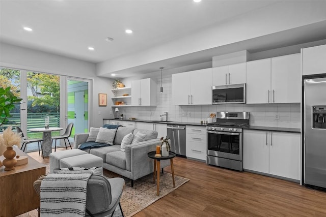 kitchen with stainless steel appliances, open floor plan, backsplash, dark wood-style floors, and dark countertops