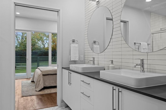 full bathroom with double vanity, wood finished floors, a sink, and decorative backsplash