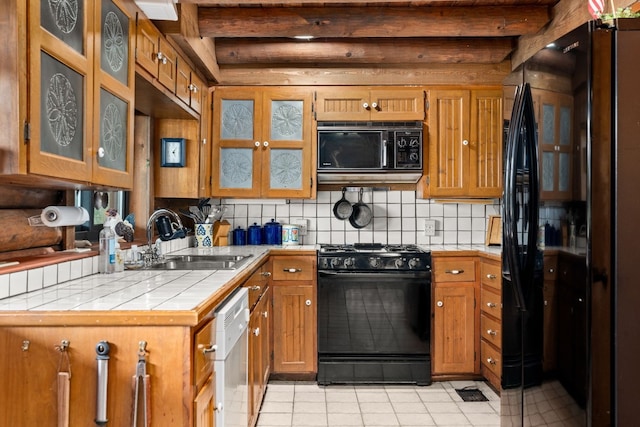 kitchen with decorative backsplash, tile countertops, brown cabinets, black appliances, and a sink