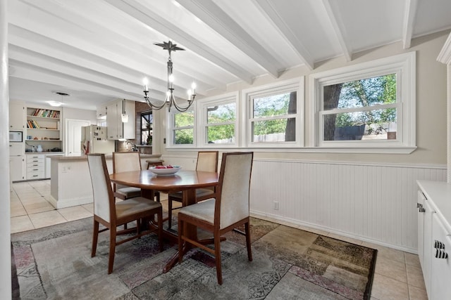 dining area featuring a wainscoted wall, a notable chandelier, light tile patterned floors, and beamed ceiling