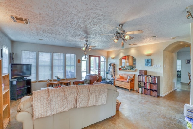 living room with baseboards, visible vents, a ceiling fan, arched walkways, and a textured ceiling