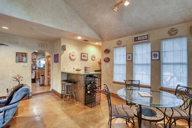 dining space featuring a dry bar, baseboards, arched walkways, a textured wall, and finished concrete floors